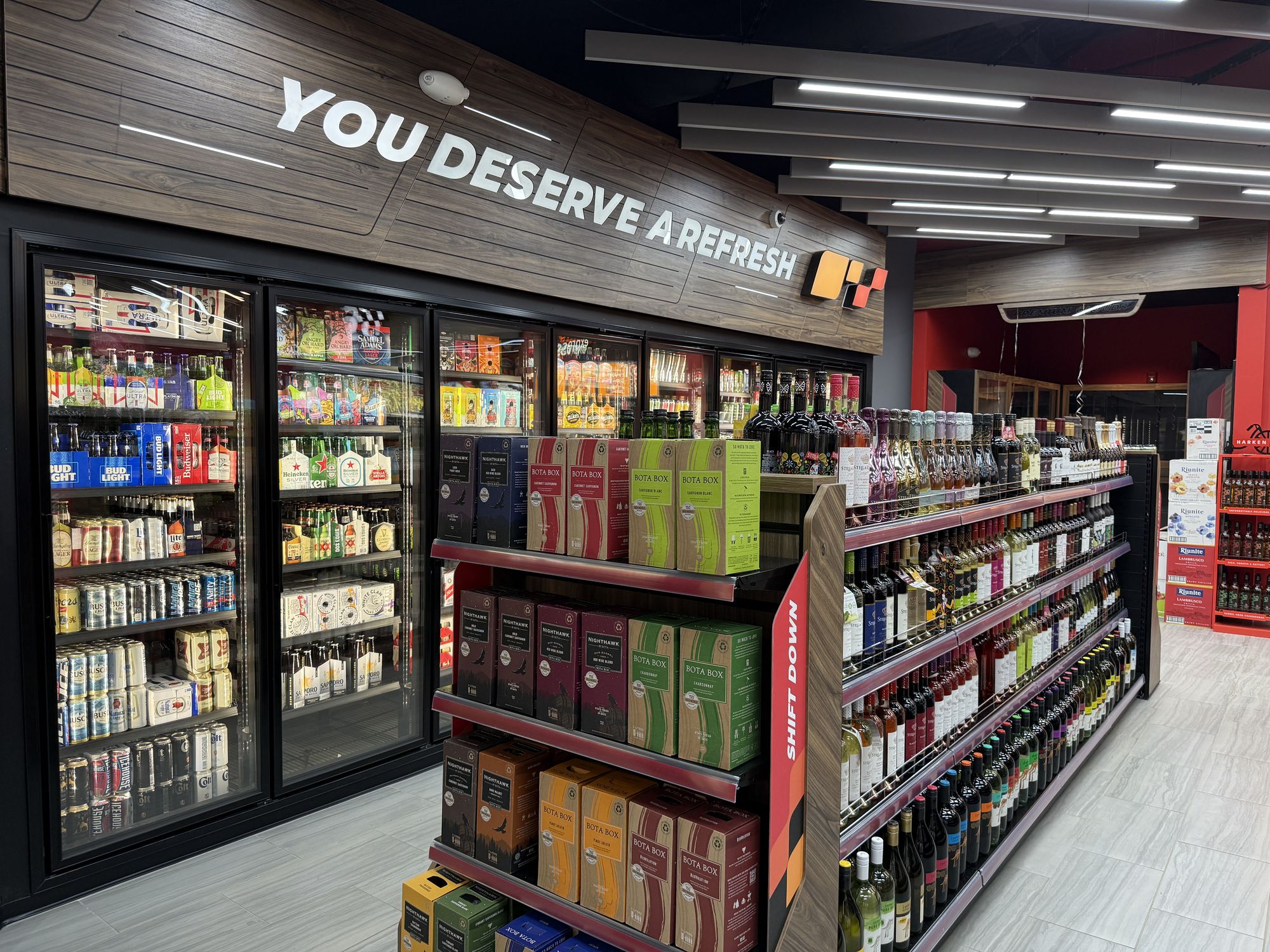 The cold vault: glass doors full of drinks under a wood bulkhead that reads You Deserve a Refresh, with the wine aisle beside it